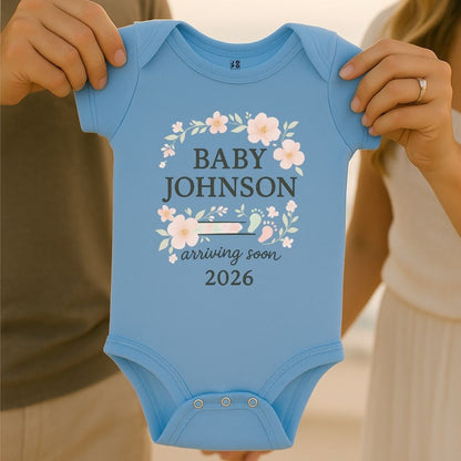 Pastelblue baby onesie with 'Baby Johnson arriving soon 2026' text with floral and baby footprint graphic design