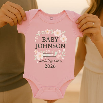Pink baby onesie with 'Baby Johnson arriving soon 2026' text with floral and baby footprint graphic design