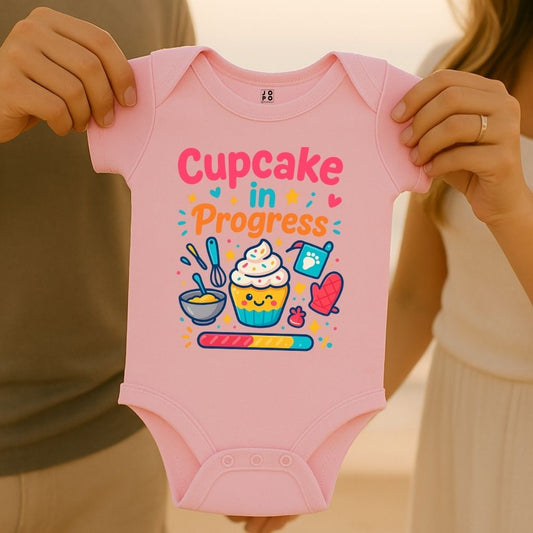 Pink baby onesie with 'Cupcake in Progress' text and cartoon-style cupcake design with loading bar graphic